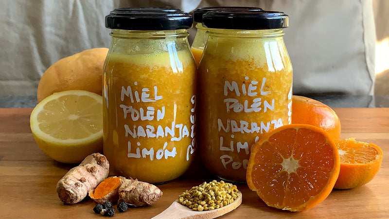 Frascos de miel con polen y cítricos junto a medio limón, naranjas, cúrcuma y una cuchara con polen