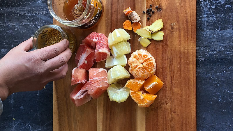 Frasco de miel Valymu con cuchara de madera junto a polen, pomelo, limón, mandarina, jengibre y cúrcuma