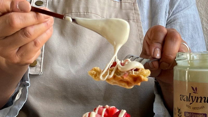 Cucharada de miel cremada Valymu cayendo sobre un trozo de waffle, junto al frasco